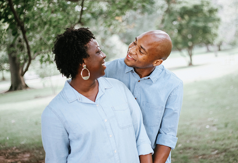 Black couple smiling at each other against a backdrop of trees