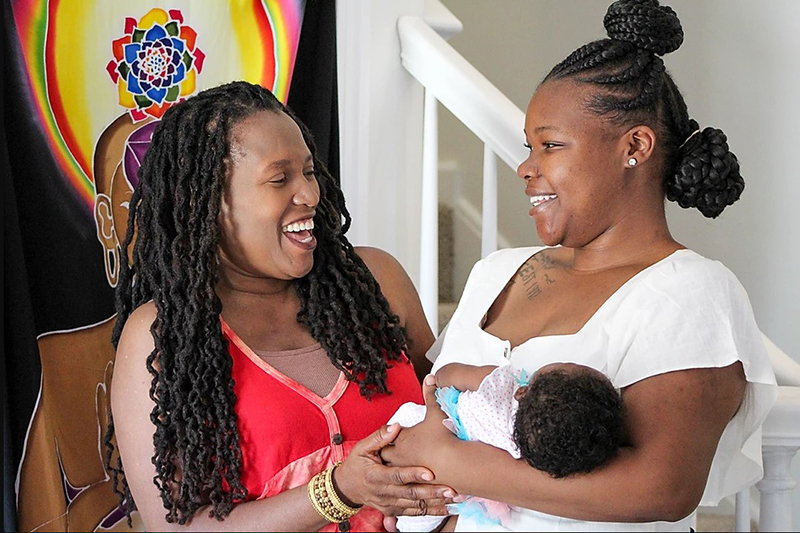 Two African American women smiling at each other, while one holds newborn