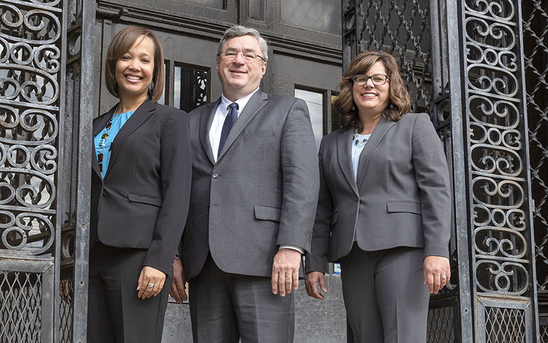 Three business people in suits pose for photo