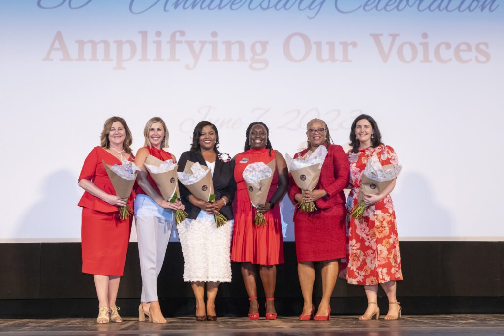 Six women standing on a stage smiling and holding bouquets of flowers at Women's Endowment Fund of Akron Community Foundation event