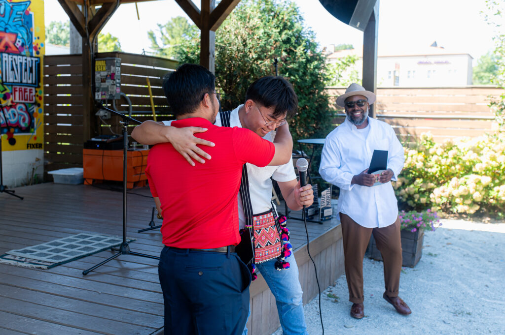 Two people hug before one receives an award while another person holds the award.