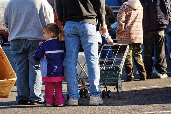 Toddler girl stands next to father in line at foodbank