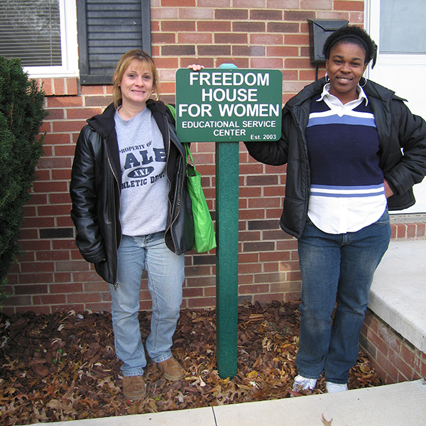 Two women standing next to Freedom House for Women sign