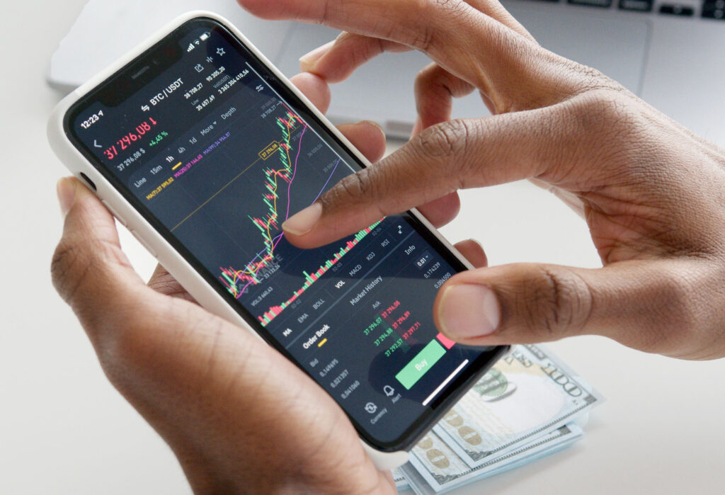 Hands holding a cell phone with stock charts on the screen