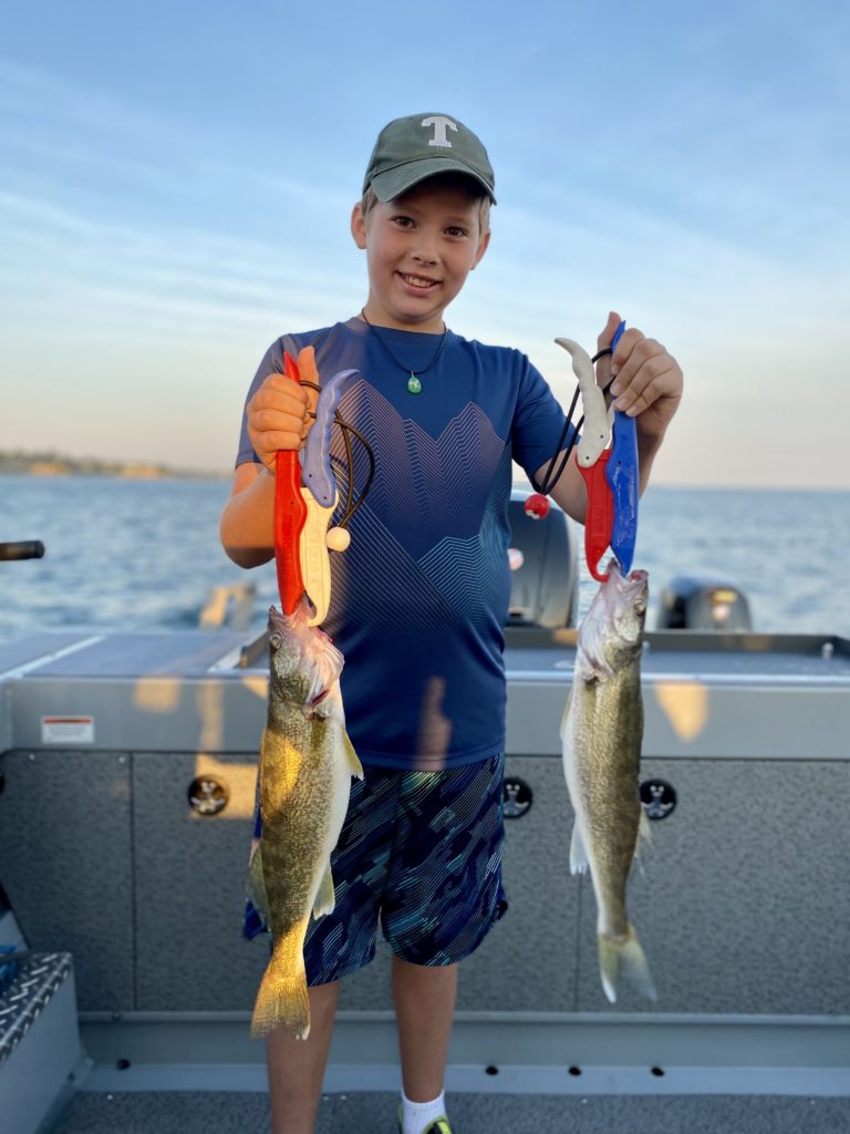 A young boy is smiling on a boat while holding two fish.