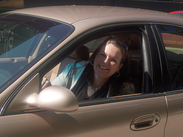 Woman in front seat of car smiles through window