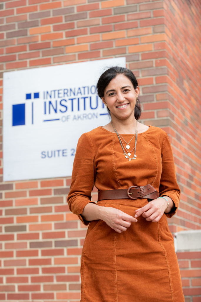Woman in orange dress smiles in front of International Institute sign