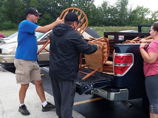 Two men and a woman load wooden chairs into the bed of a black pick-up truck