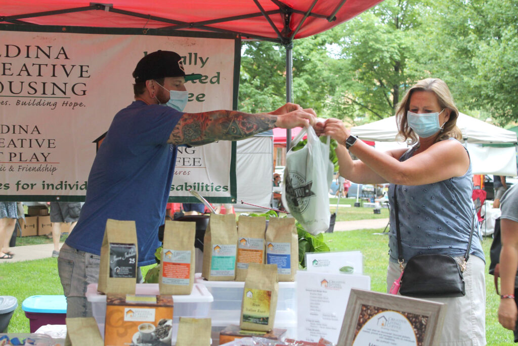 A man wearing a mask hands a bag of produce to a woman wearing a mask.