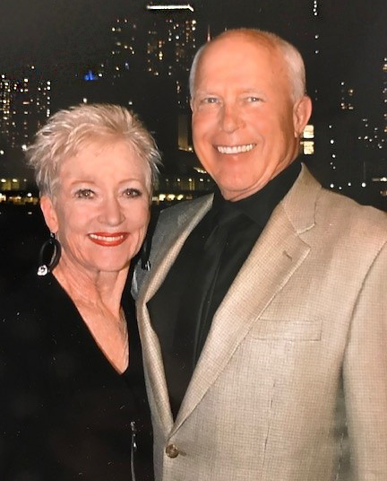 Cheryln Nilsen and her husband smile for a photo together in front of a dark city backdrop.