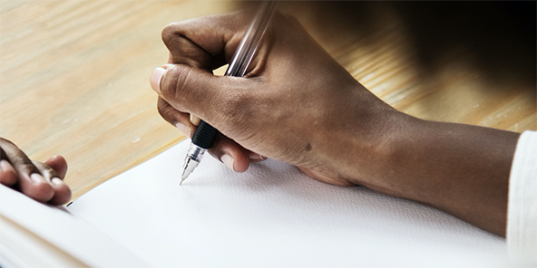 Person's hand, holding a pen and writing in a notebook