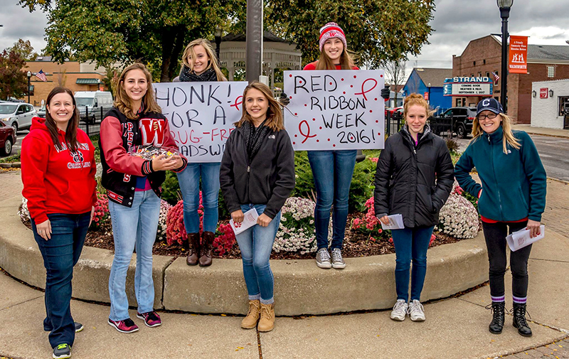 Group of girls stand on curb holding Red Ribbon Week signs