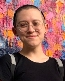 Sam Caley smiling in front of a colorful mural on a brick wall