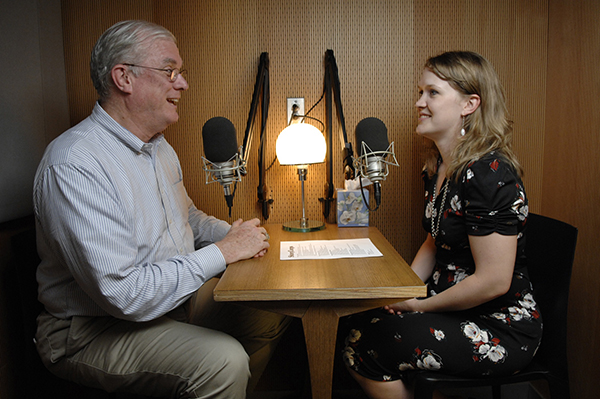 Man and woman sitting across from each other speaking into microphones