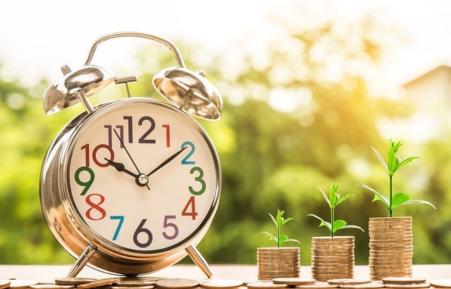 Alarm clock next to stacks of coins with plants growing