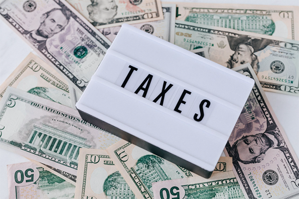 A letter board reading 'TAXES' is laid across a pile of money.