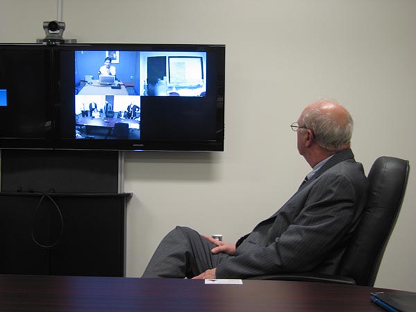 Man in office chair watches videoconference on TV