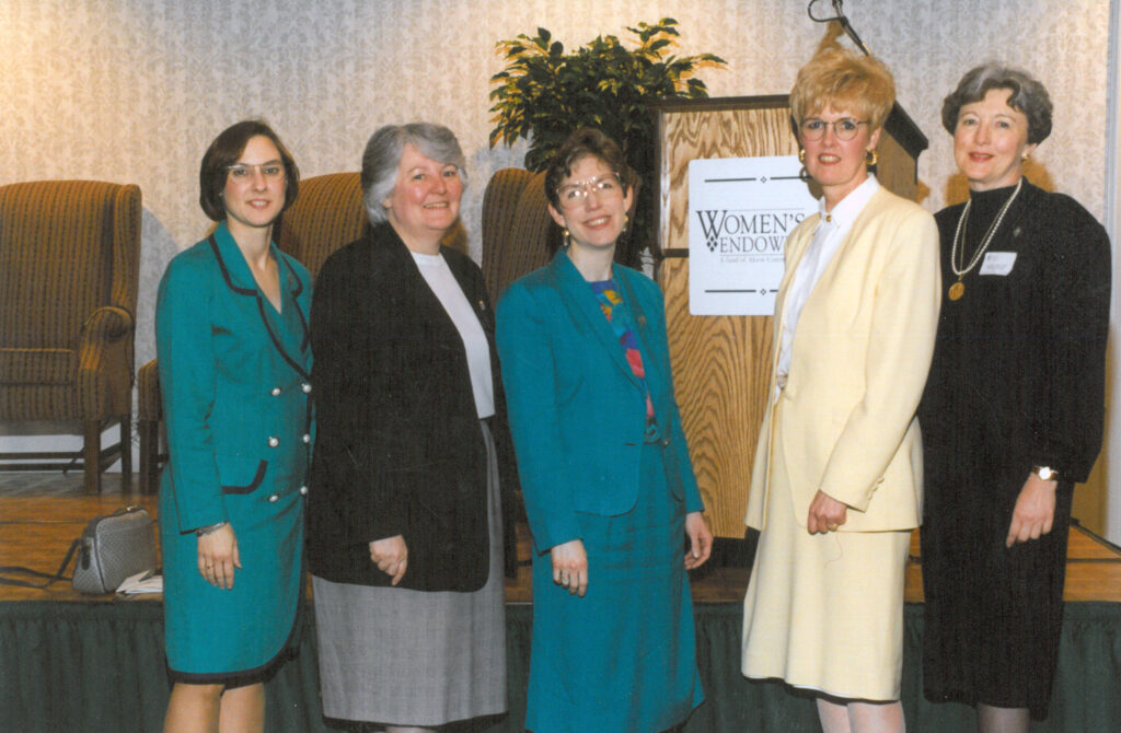 A group of five women smile for a photo in front of a podium