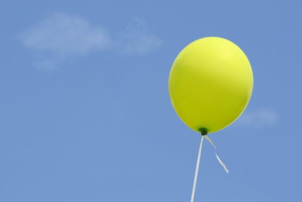 a yellow balloon with a white string attached in front of a blue sky