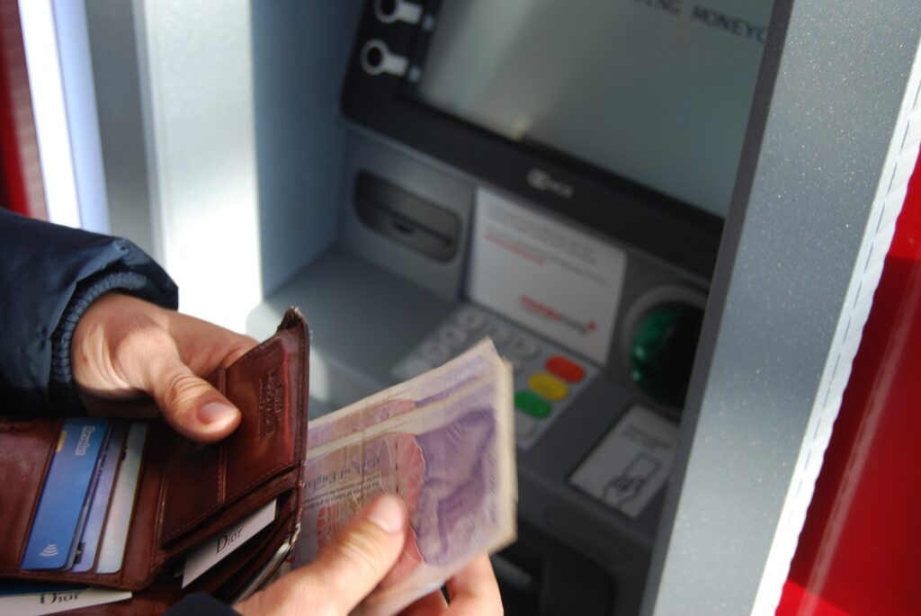 Person holding wallet and cash in front of an ATM