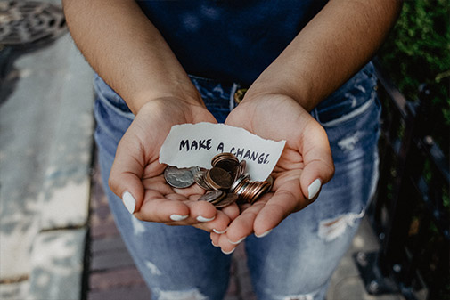 woman holding a note that reads 'MAKE A CHANGE.' and a pile of coin change