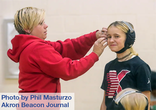 A woman adjusts a wrestling helmet on a young girl's head