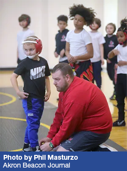 A Kenmore Wrestling Club coach ties a wrestler's shoes