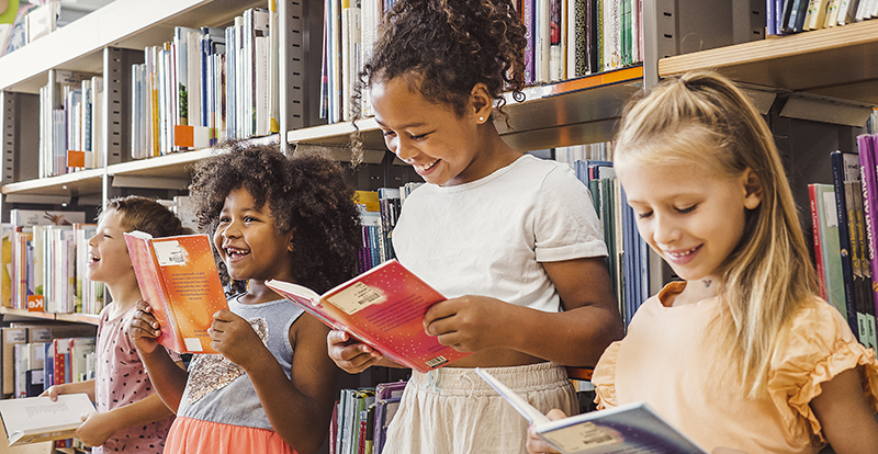 Kids reading books in front of library shelves