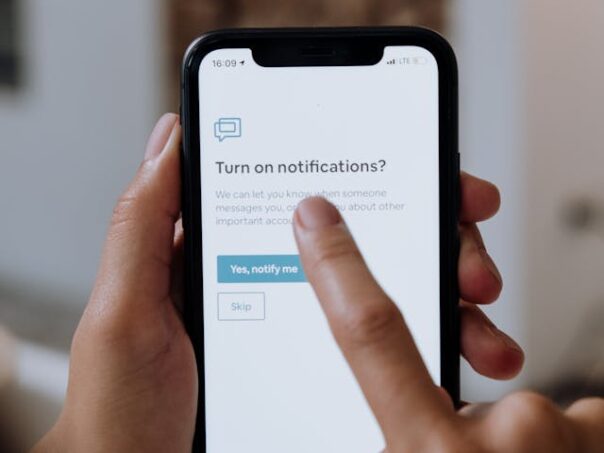 A phone is held in one hand while pointing at screen notifications.