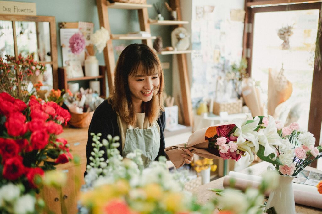 Smiling woman in an apron surrounded by flowers in a flower shop.