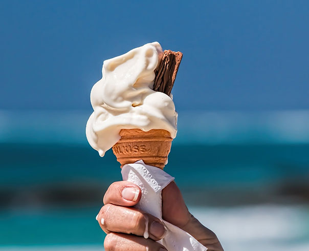 A hand is holding an ice cream cone, which is wrapped in a napkin and starting to melt. 