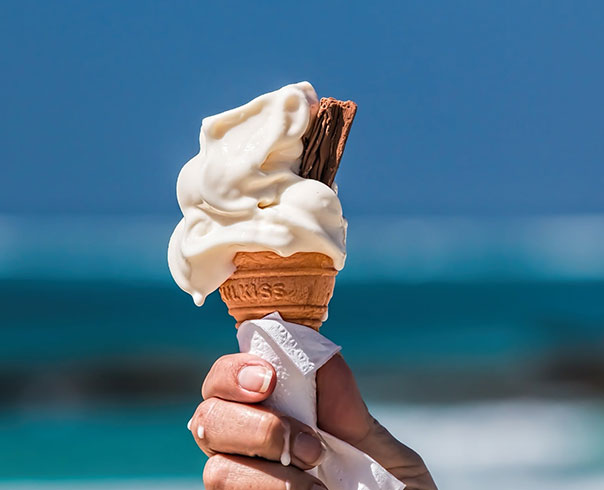 A hand is holding an ice cream cone, which is wrapped in a napkin and starting to melt.