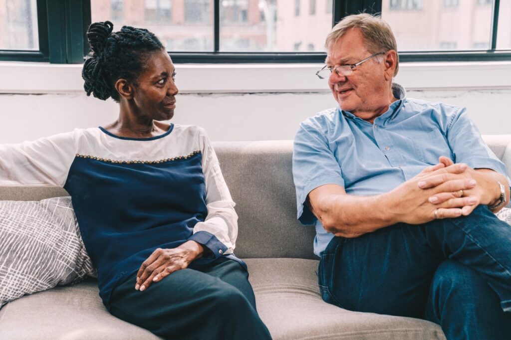 Black woman and older white man conversing on a couch